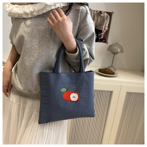 Detailed close-up of blue nylon tote bag with red apple embroidery on a wooden table