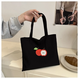 Close-up of red apple embroidery on a black nylon tote bag with handle detail