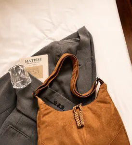 Detail of a brown suede hobo bag with a woven knot zipper pull on a grey blazer