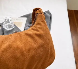 Detail showing the brown suede hobo bag texture and zipper closure on a white bed