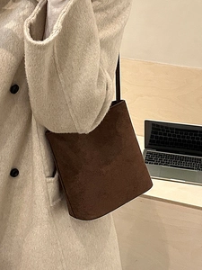 Retro dark brown suede bucket bag worn over a wool coat in a stylish office setting