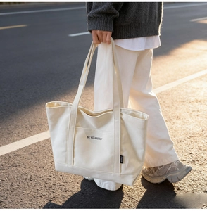Detail of off-white canvas tote bag featuring black BE YOURSELF text and side label