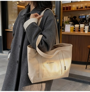 Detail view of the BE YOURSELF printed canvas tote bag in beige with side brand label