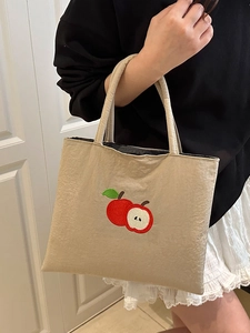 Minimalist beige nylon tote bag with red apple embroidery shown in a hand-held view