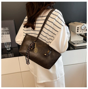 Detail of dark brown leather tote bag with woven pendant and golden tennis racket charm