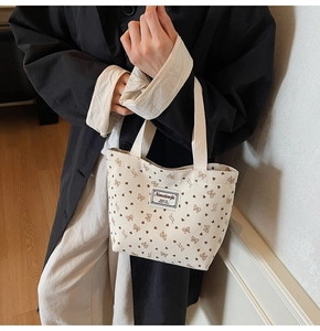 Detail of cream corduroy tote bag featuring brown bow prints and woven brand label