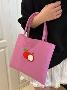 Pink nylon tote bag with red apple embroidery worn by a model in a minimalist setting