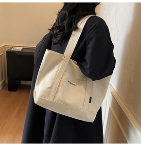 Detail of off-white canvas tote bag with 'BE YOURSELF' text and side logo tag