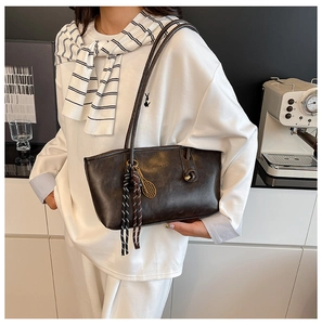 Detail of a large brown tote bag with striped ribbon and gold pendant on a model's shoulder