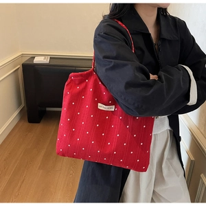 Detail shot of a red floral canvas tote bag featuring a white brand label and textile texture