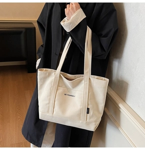 Close-up of minimalist cream canvas tote bag featuring BE YOURSELF print and side pocket