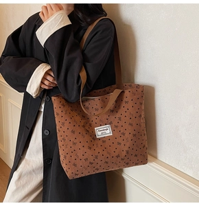 Detail view of brown corduroy tote bag with heart and bow patterns on black wool coat