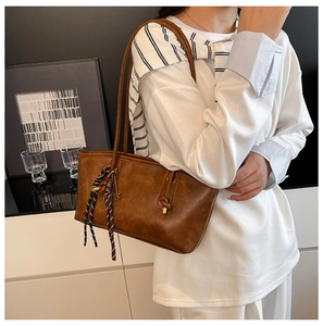 Close-up of vintage brown leather tote bag with silk scarf charm and embossed logo detail