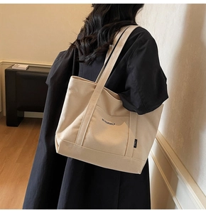 Detail of beige canvas tote bag featuring BE YOURSELF lettering and large front pocket