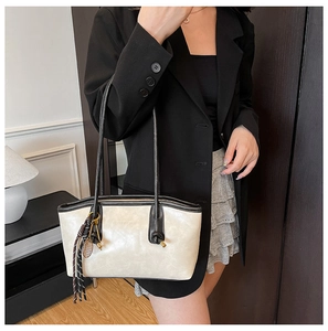 Detail of beige tote bag with black piping, fringe tassel and metallic racquet charm