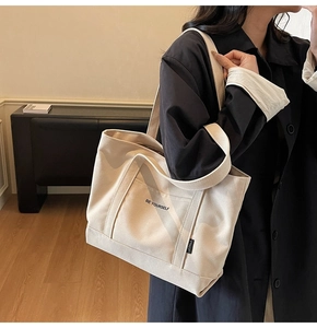 Close-up of cream canvas tote bag with 'BE YOURSELF' text and woven logo tag