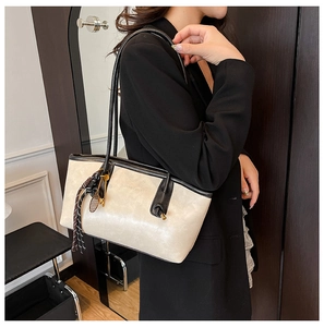 Detail of beige tote bag with black trim and racket charm accessory on model shoulder