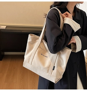 Detail of cream canvas tote bag featuring BE YOURSELF print and outer pocket on shoulder