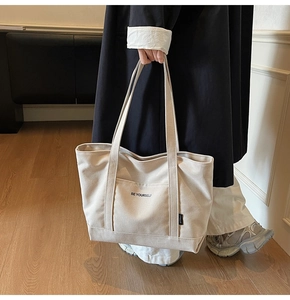 Detail of canvas tote bag with front pocket and printed BE YOURSELF text and small black label