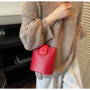 Detail of red woven leather bucket bag featuring a magnetic clasp and fine shoulder strap