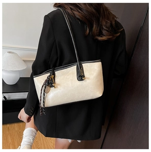Detail of a large cream-colored tote bag with black trim and tassel worn by a model