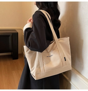 Detailed side view of beige canvas tote bag with Be Yourself lettering on female model