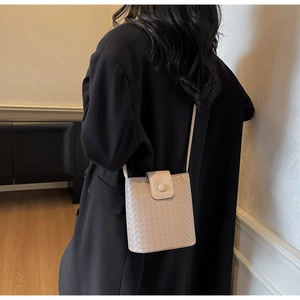Detail view of beige woven bucket bag worn over a black blazer for a stylish look