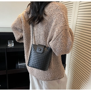 Detail of a black woven leather bucket bag with a round buckle closure and shoulder strap