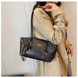 Detail of a large black vintage tote bag with woven pendant on khaki trench coat
