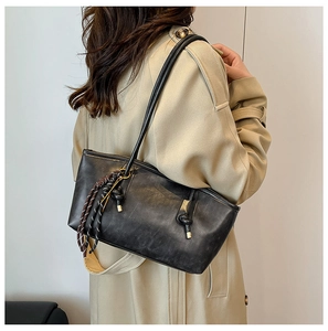 Detail of vintage black leather tote bag featuring stylish knot and braided charm