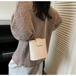 Detail of white woven bucket bag showing textured synthetic leather and a crossbody strap