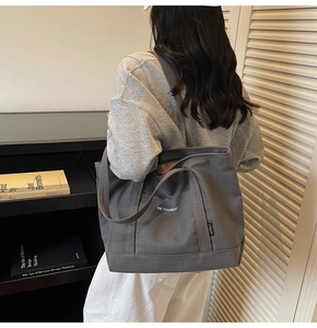 Detailed view of the thick canvas texture and 'BE YOURSELF' print on the gray tote bag