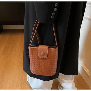 Detail of a brown woven bucket bag with magnetic closure and adjustable strap