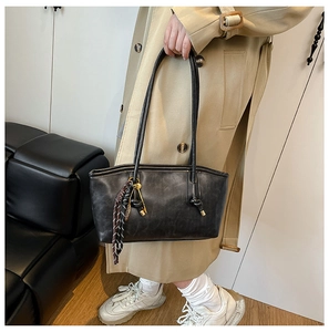 Detail of black leather tote bag with vintage silk scarf charm on khaki trench coat