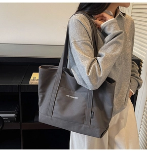 Close-up of dark grey canvas tote bag with Be Yourself print and front pocket detail