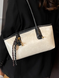 Retro cream tote bag with black trim and long shoulder straps worn with a black blazer