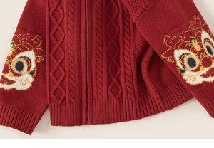 Détail du cardigan en maille rouge avec motif torsadé et broderie de lion sur la manche