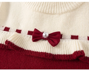 Détail d'un nœud rouge avec perle et volants en tricot sur une robe de fête enfant