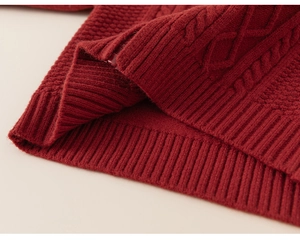 Détail d'un pull en maille torsadée rouge montrant la texture et l'ourlet côtelé