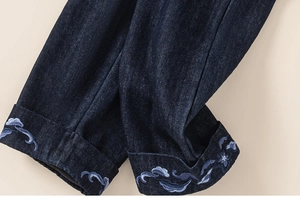 Detail of dark blue denim cuff with intricate light blue sea wave embroidery detail