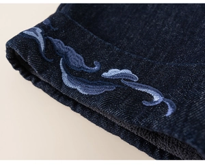 Detailed macro view of dark blue denim hem featuring traditional light blue cloud embroidery