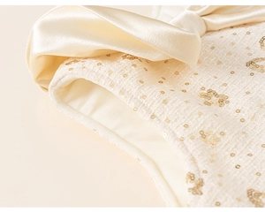 Détail d'une robe en tweed avec paillettes dorées et un nœud en satin crème