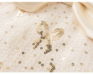 Détail du tissu en tweed avec paillettes dorées et nœud en satin sur vêtement enfant