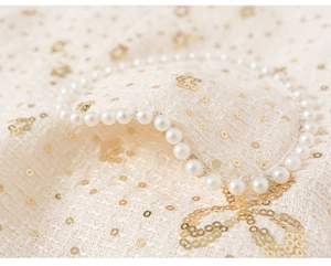 Détail du tissu en tweed avec paillettes dorées et perles blanches pour robe enfant