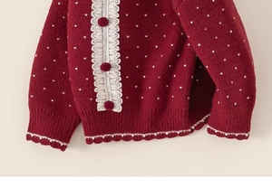 Detail of red knitted girl sweater with white polka dots and delicate lace trim