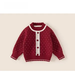 Detail of red girls' knit cardigan with white polka dots, lace trim, and pom-pom buttons