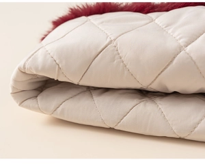 Close-up of quilted vest with plush burgundy faux fur lining and beige diamond stitching