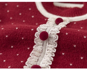 Detail of red knit sweater featuring white polka dots and lace trim with pom-pom buttons