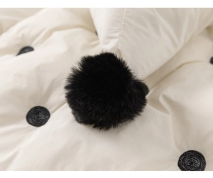 Detail of baby winter coat showing beige fabric with black dots and soft pompom texture