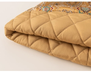 Detail of golden diamond quilted fabric and vintage floral embroidery on winter dress